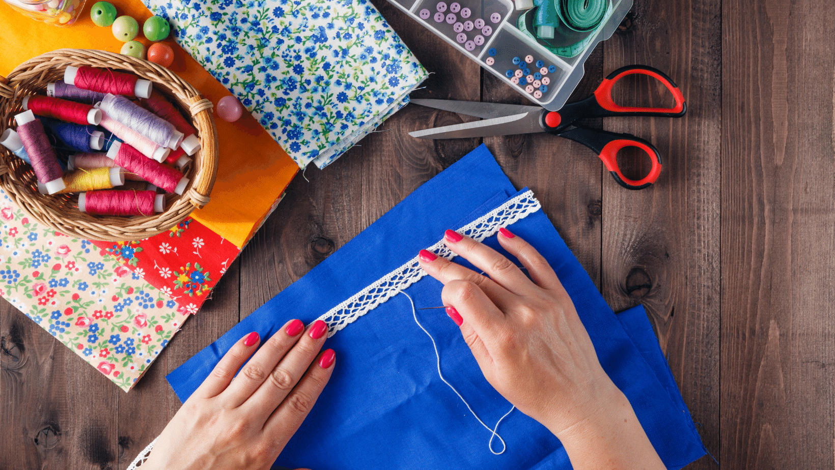 Hand Sewing Photo This photo shows how to hand sew. Top view with a basket of assorted threads, scissors, hand hand sewing a white scallop trim to one edge of a blue fabric.
